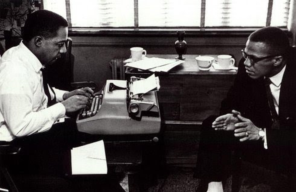 Alex Haley sitting at a typewriter while Malcolm X talks across the desk